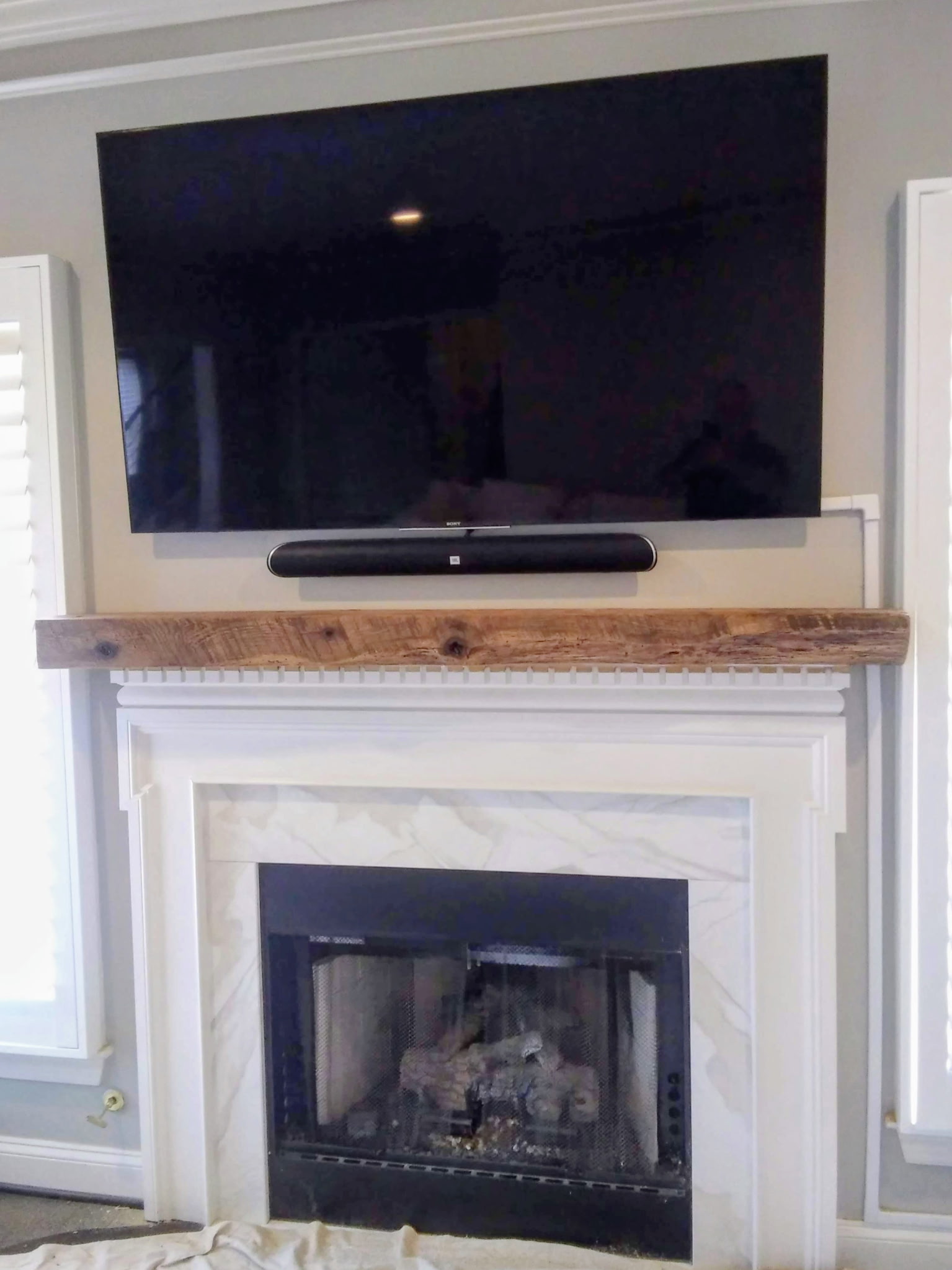 Reclaimed wood beam mantel over a white marble fireplace